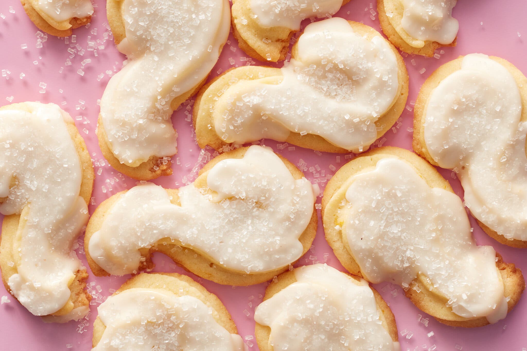 Several curled cookies frosted with icing sit on a pink background.