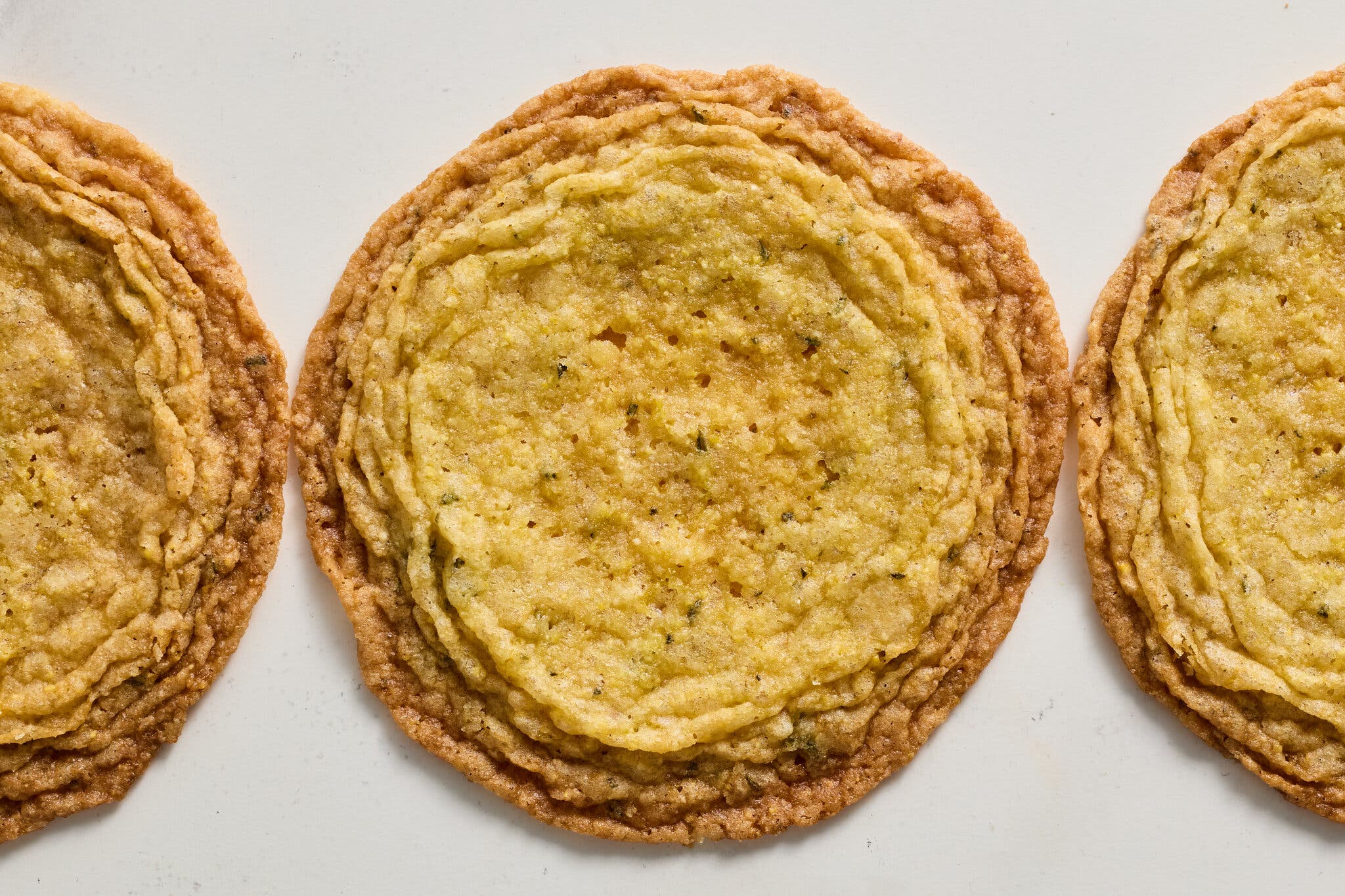Three crinkle-edged yellow cookies sit on a beige surface.