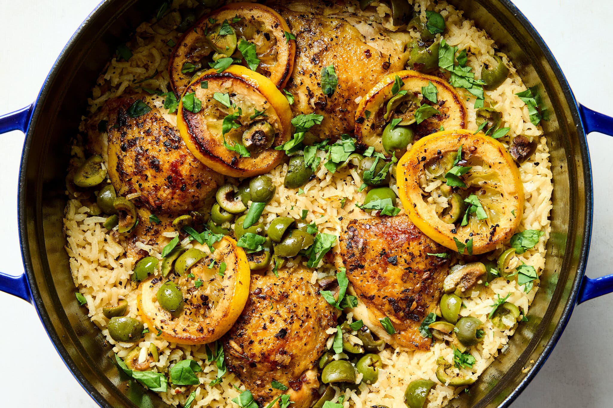 A Dutch oven filled with rice, chicken, olives and lemon slices.