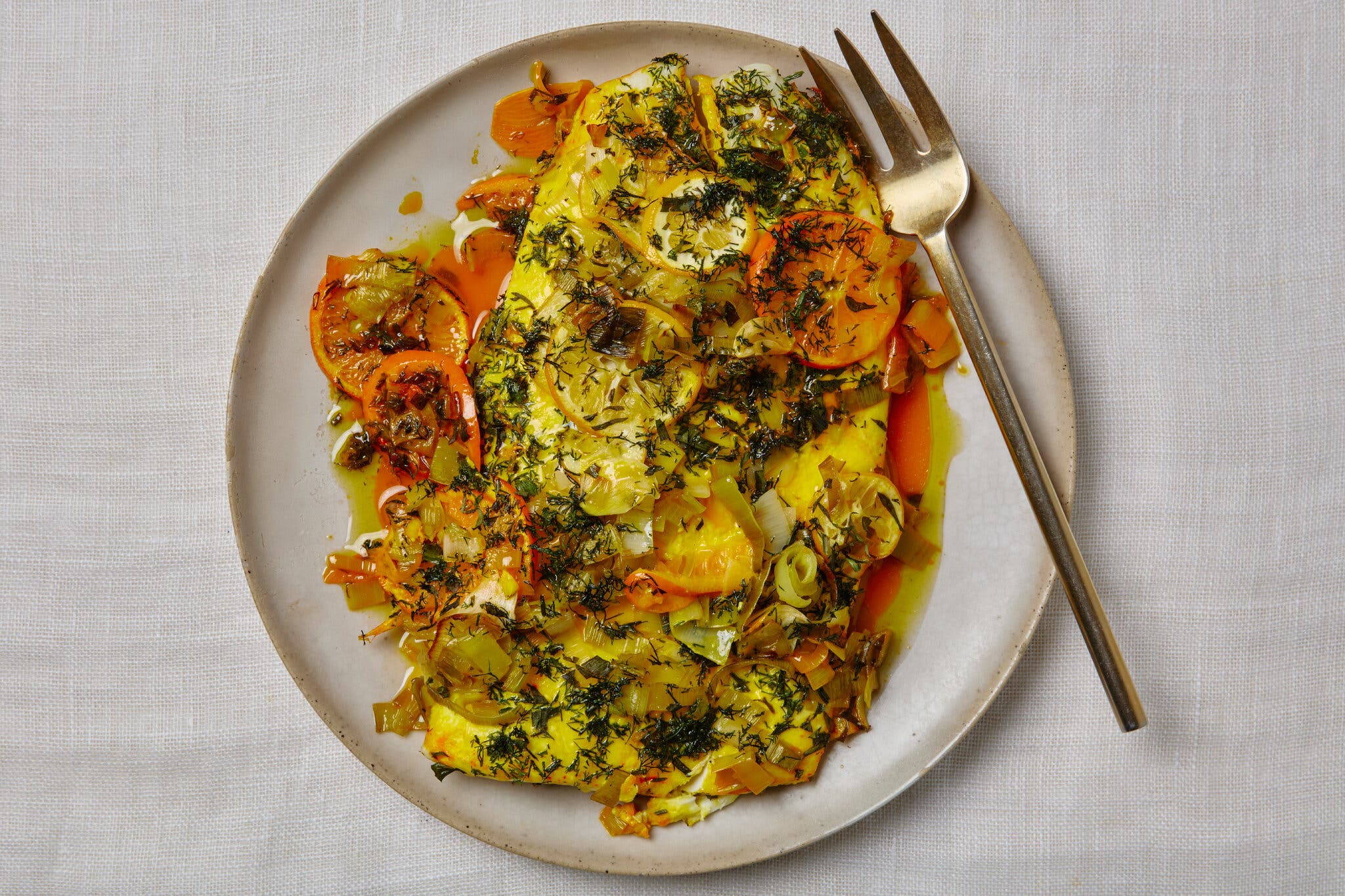Fish covered in herbs and sliced citrus sits on a plate.