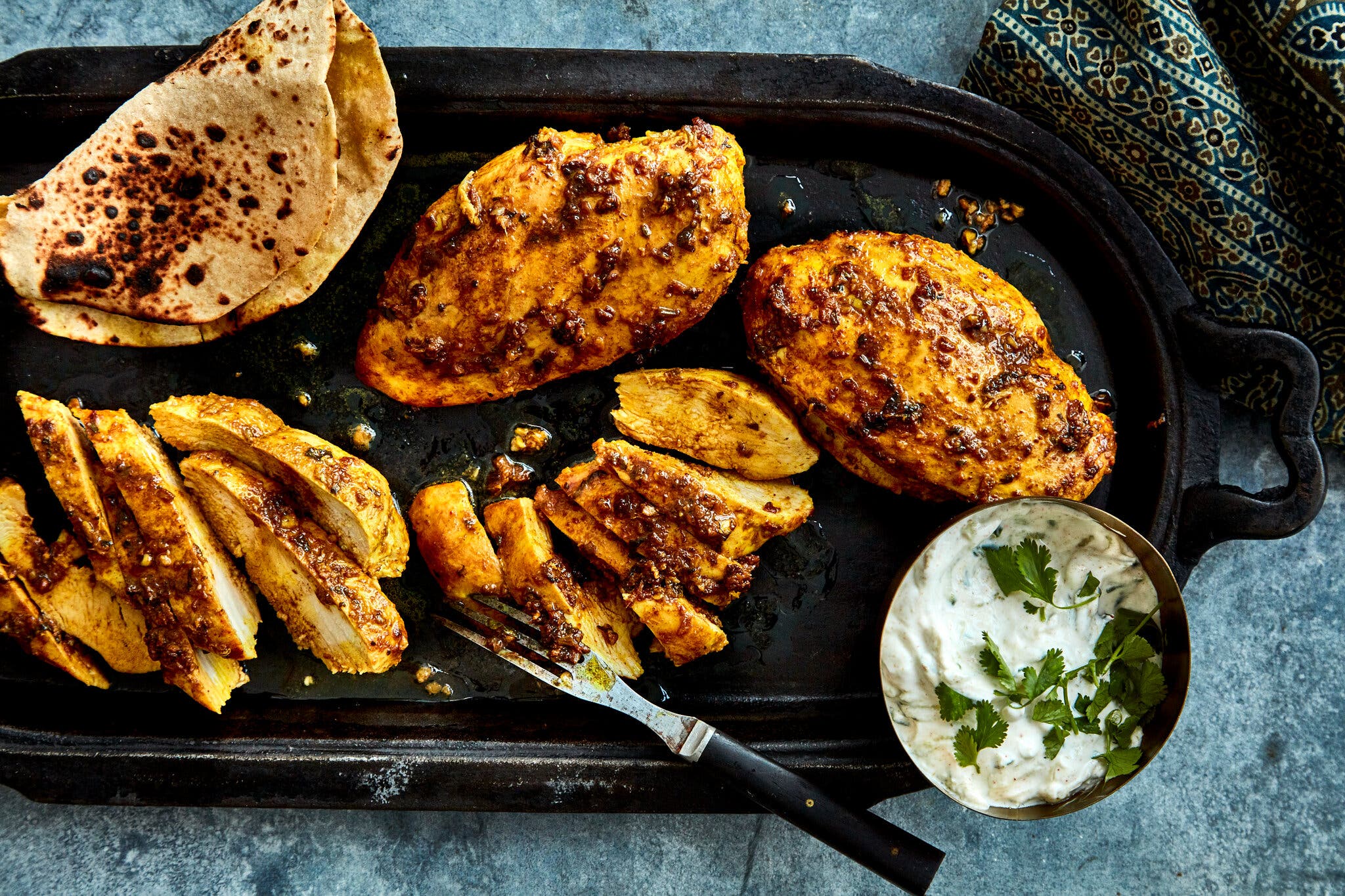 An overhead image of chicken breasts on a griddle next to a creamy sauce.