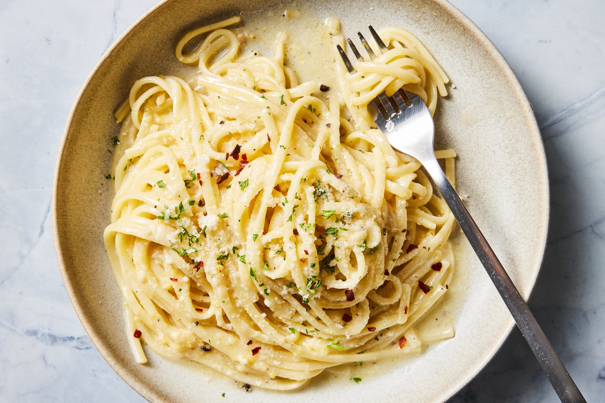 A fork with a swirl of pasta on it sits on a ceramic plate filled with more pasta.