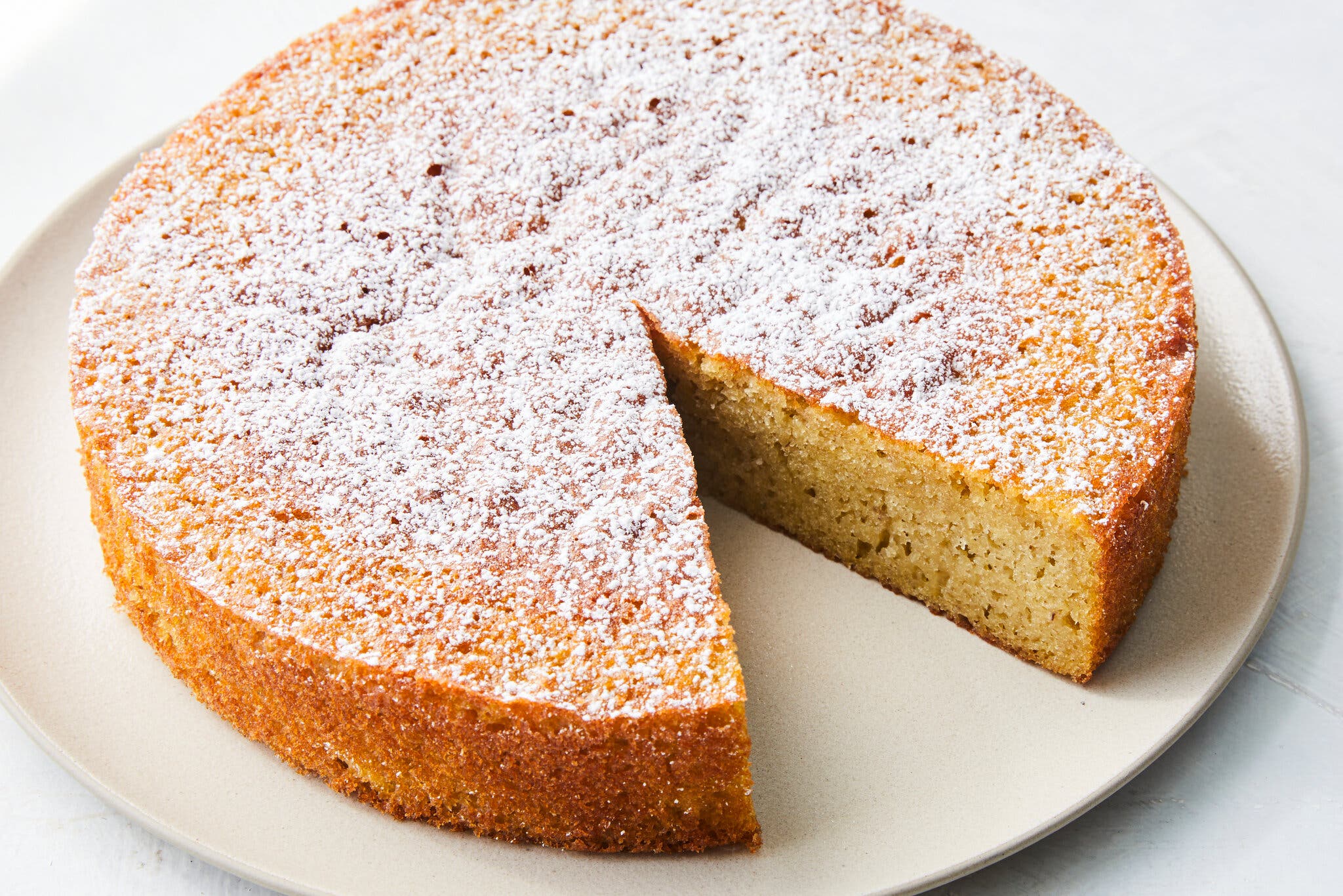 A lemony olive oil cake is photographed from the side with a slice missing.