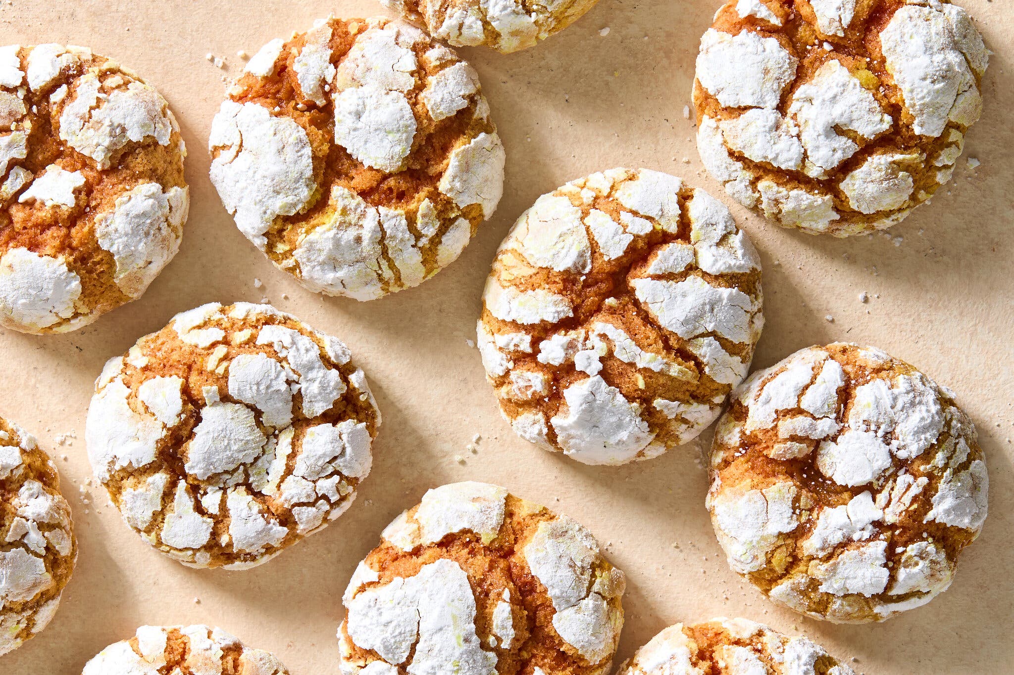 Cookies with deep cracks all over them and a white topping sit on a beige counter.