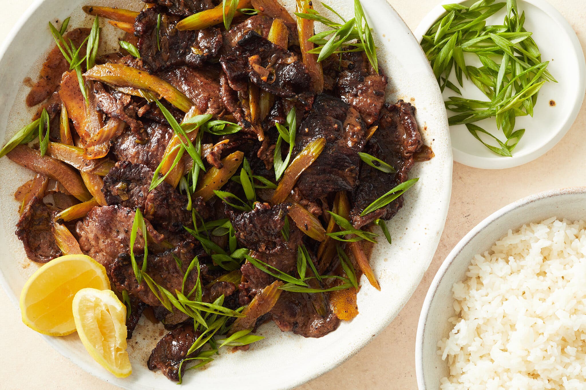 An overhead image of a beef stir-fry next to rice and slivered scallions.