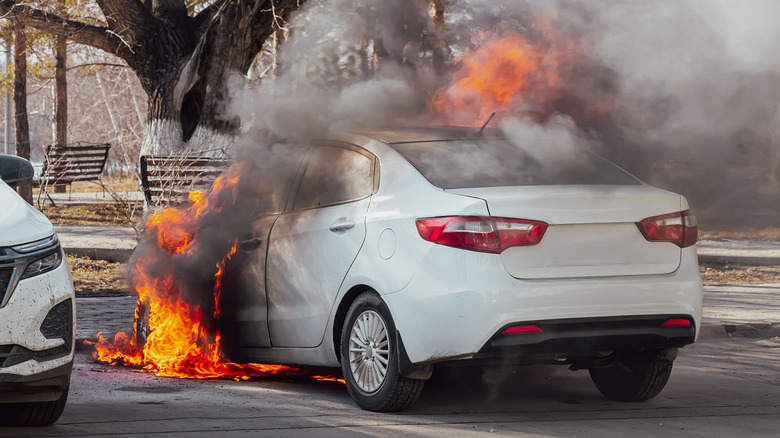 A white compact sedan with an engine fire.