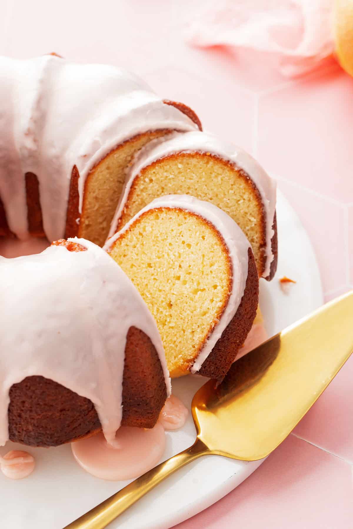 Grapefruit Olive Oil Bundt Cake with two cut slices leaning against each other, on a white cake plate with pink background.