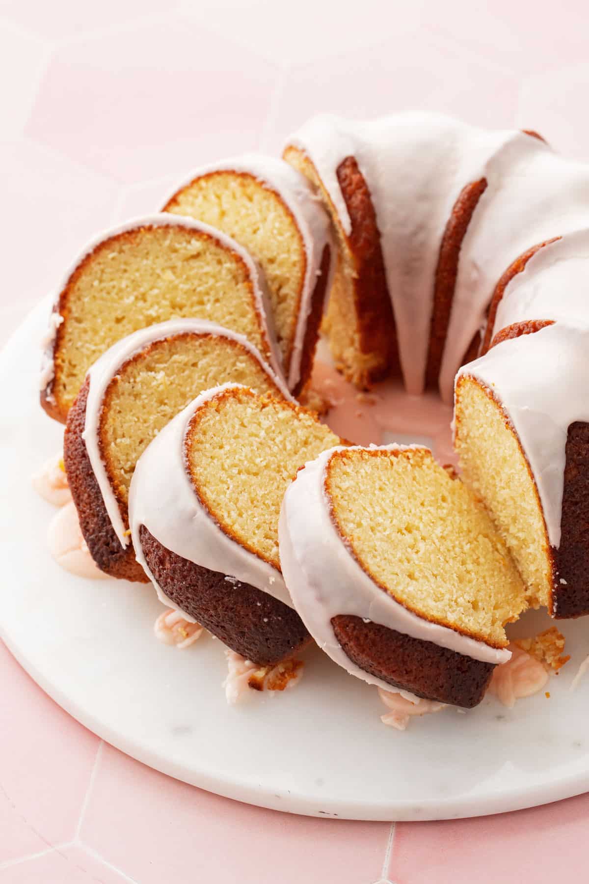 Slices cut from a glazed Grapefruit Olive Oil Bundt Cake leaning against each other, on a white cake plate with pink background.