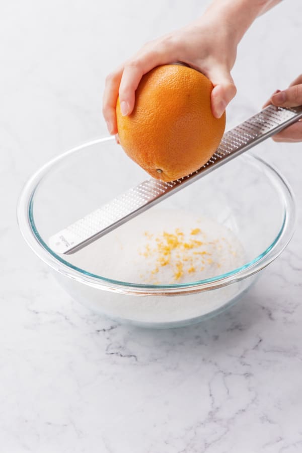 Zesting a grapefruit with a microplane over a bowl of granulated sugar.