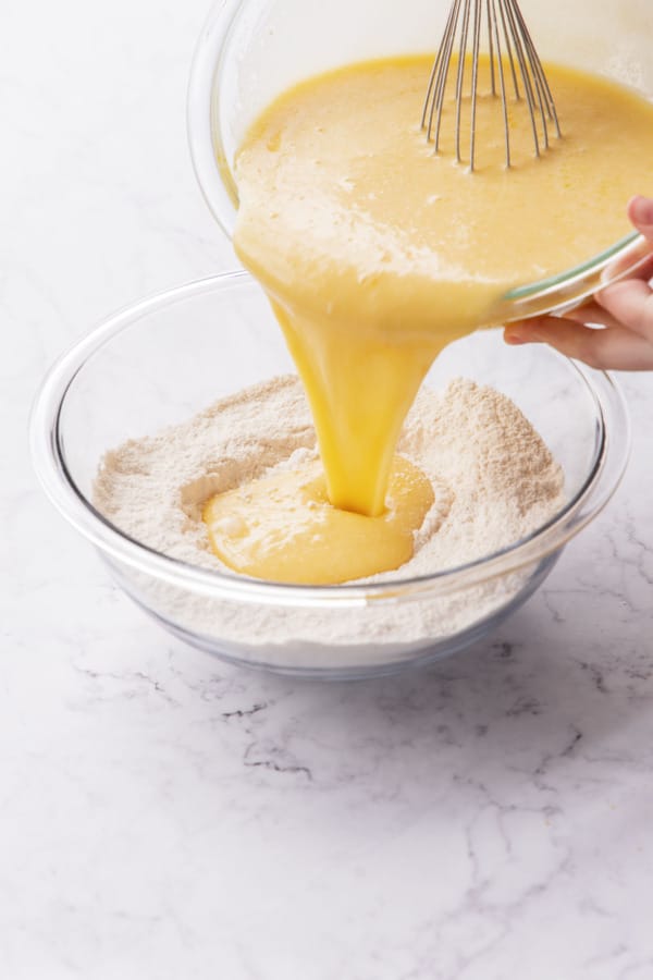 Pouring wet ingredients into mixing bowl with dry ingredients.