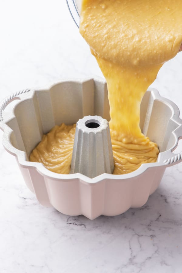Pouring grapefruit olive oil cake batter into a greased bundt pan.