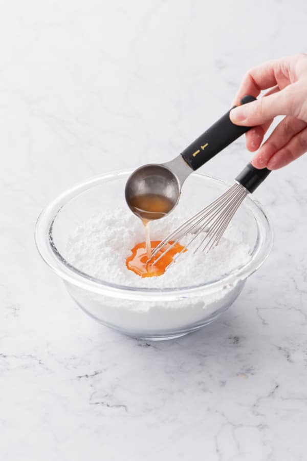 Adding grapefruit cordial to a bowl of sifted powdered sugar to make the glaze.