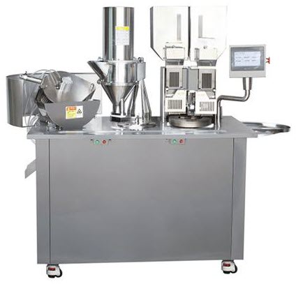 A stainless steel capsule filling machine with a control panel, hoppers, funnels, and compartments for processing and filling capsules, set on wheels for mobility.