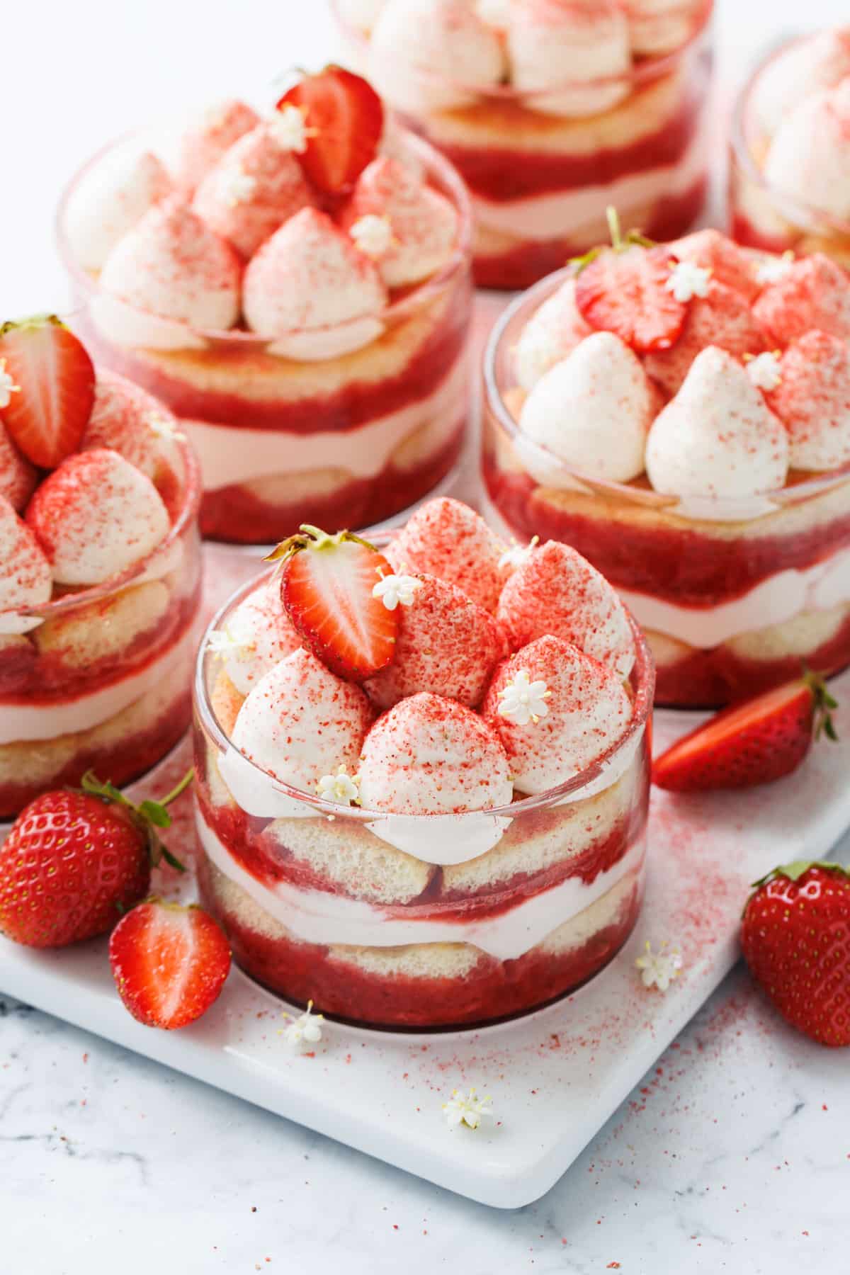Strawberry Elderflower Tiramisu in individual clear ramekins, on a white marble background with a few fresh strawberries on the side.