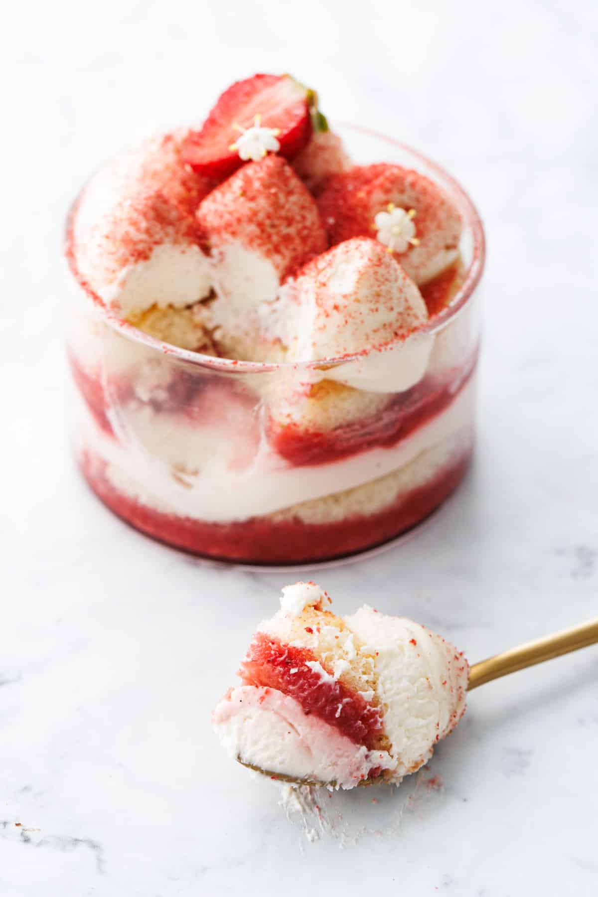 Strawberry Elderflower Tiramisu in a clear ramekin, with a spoon full sitting in the foreground to show the various layers.