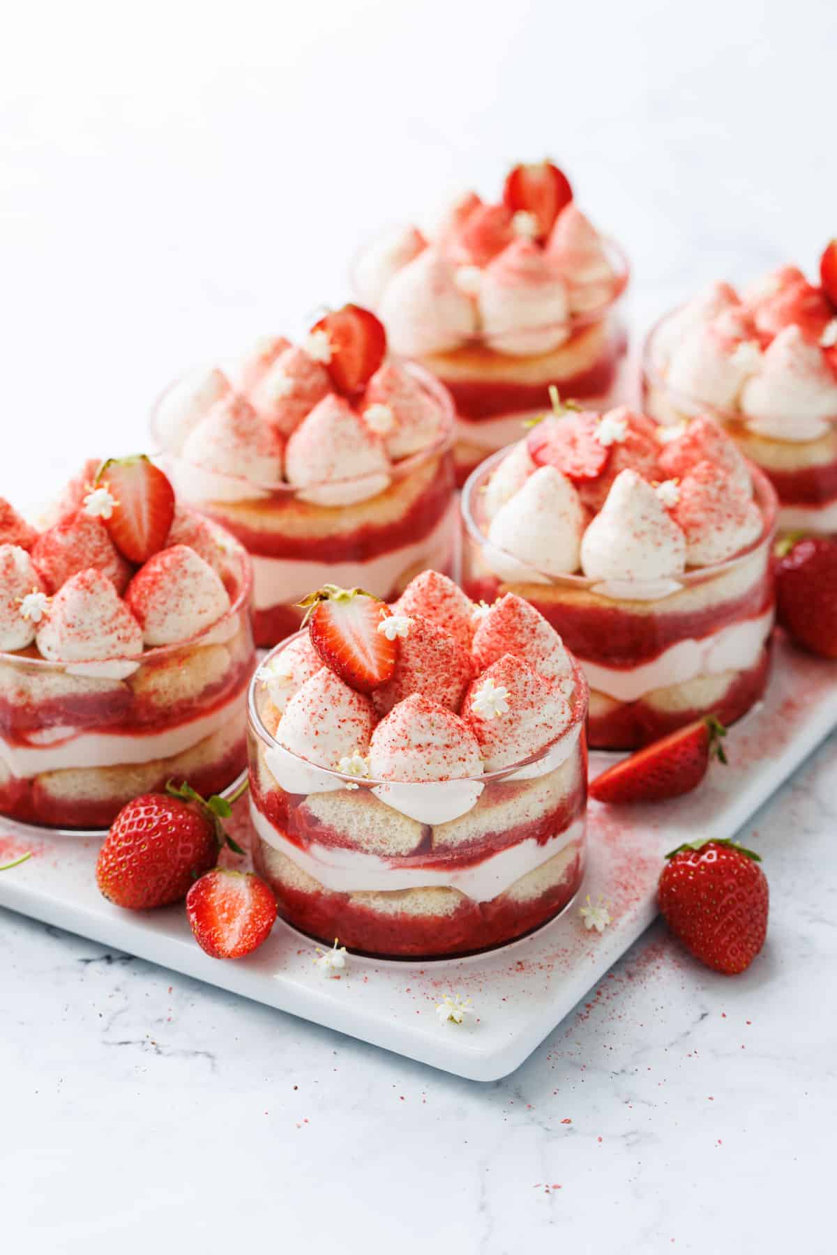 Strawberry Elderflower Tiramisu in individual clear ramekins, on a white rectangle serving plate.