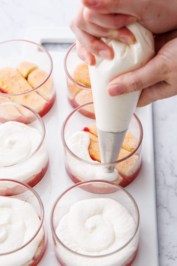 Piping the first layer of mascarpone cream on top of the ladyfingers in the ramekins.