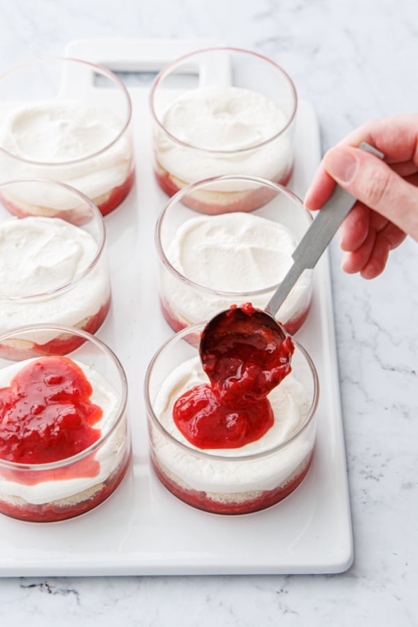 Spooning a second layer of strawberry sauce onto the mascarpone in the ramekins.