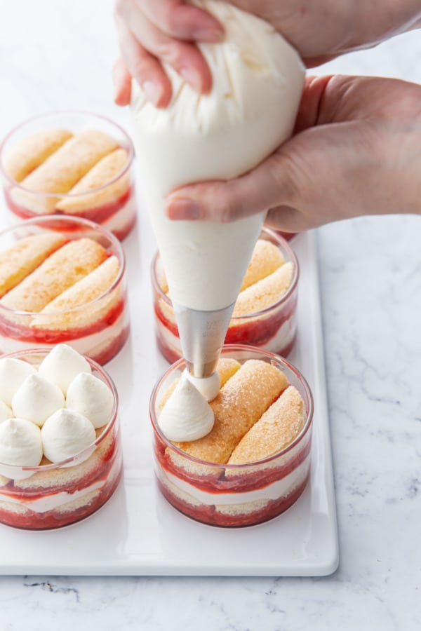 Piping dollops of mascarpone cream onto the tops of the tiramisu-filled ramekins.