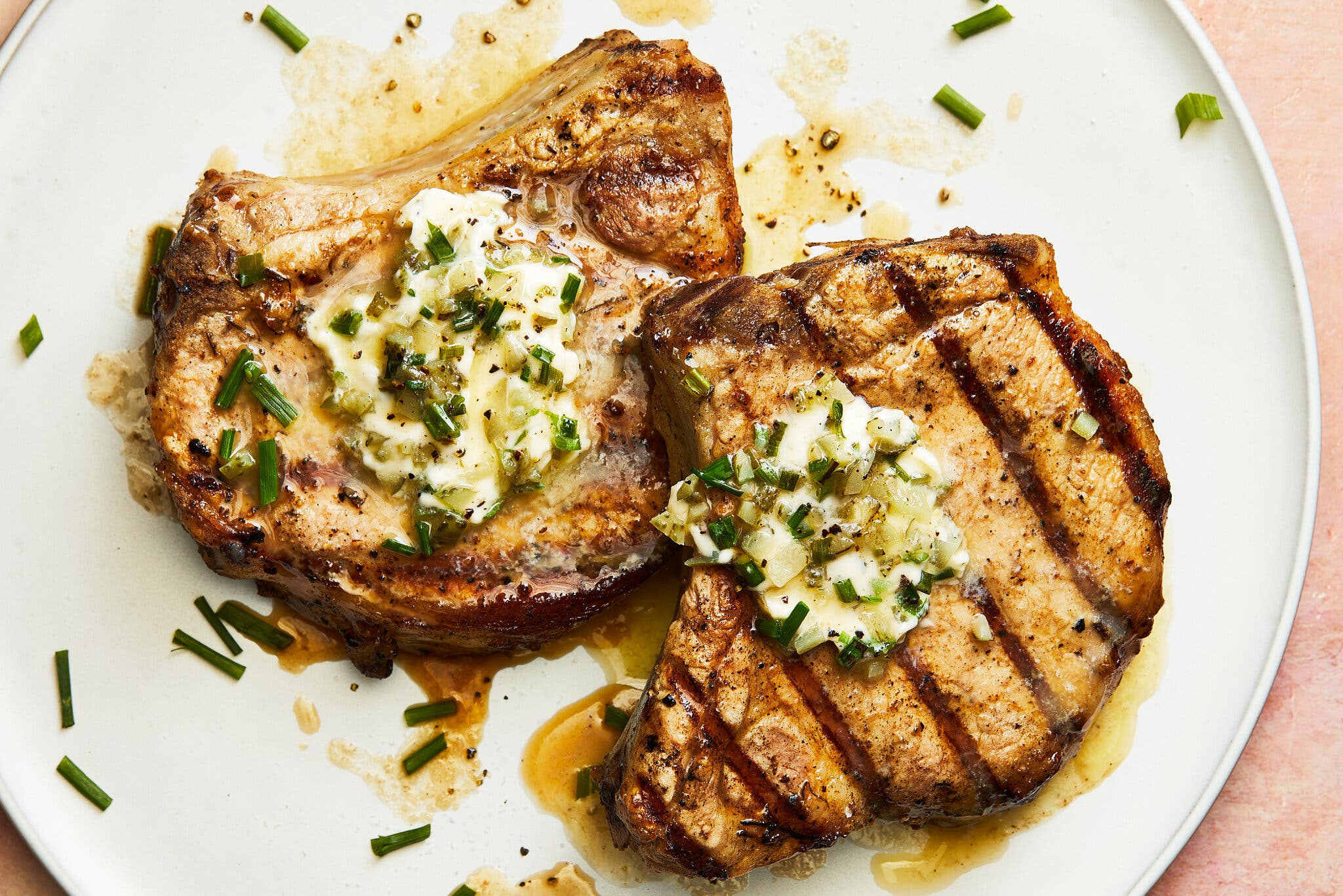 Two pork chops with grill lines top a white plate.