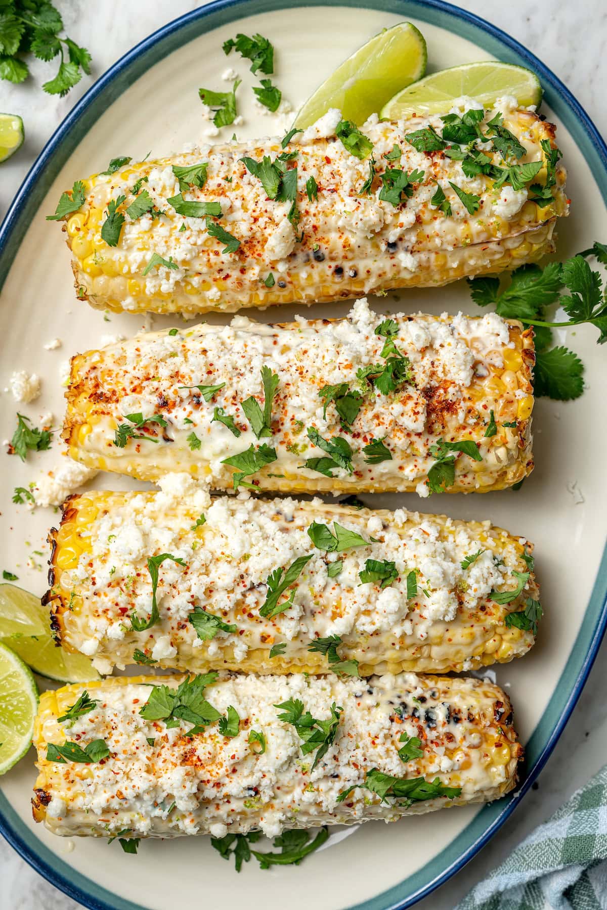 This lighter version of the classic grilled Mexican street corn recipe has all the flavor of the original, with mayo, cotija, lime and Tajín! Overhead view of 4 ears of Mexican street corn on platter with cilantro and lime wedges