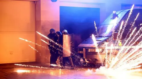 Reuters A firework exploding by a police van and three riot police huddling behind a riot shield