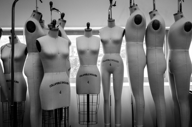 Black and white photo of a row of unclothed headless and armless female and male shaped mannequins