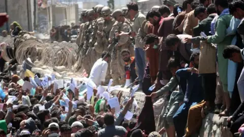 EPA A crowd of Afghans handing their papers to soldiers at Kabul Airport