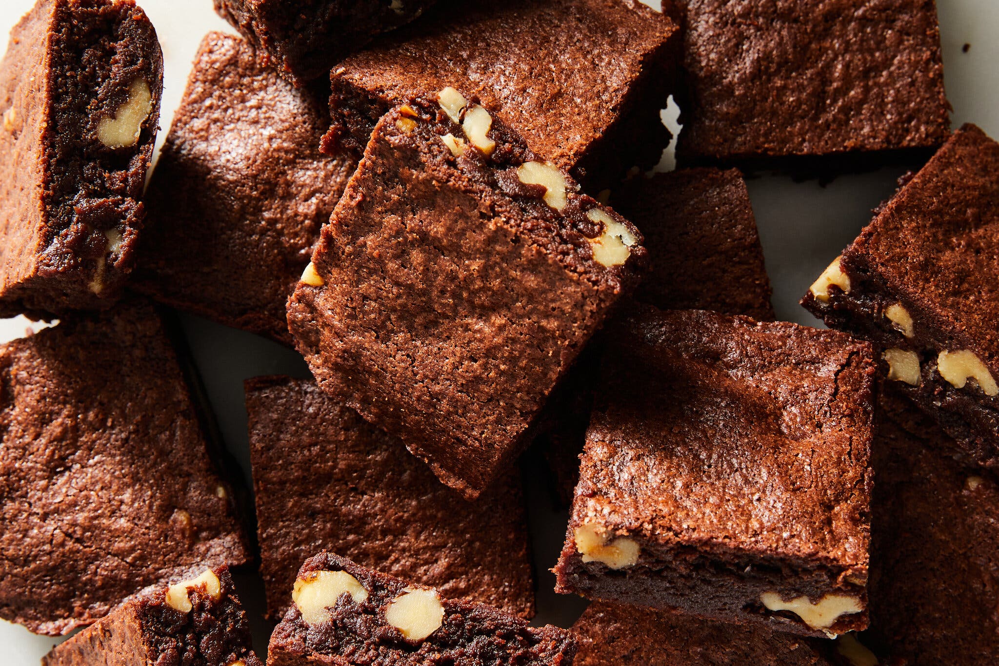 A close-up view of multiple dark brown brownies with chopped walnuts on top, arranged in a pile.