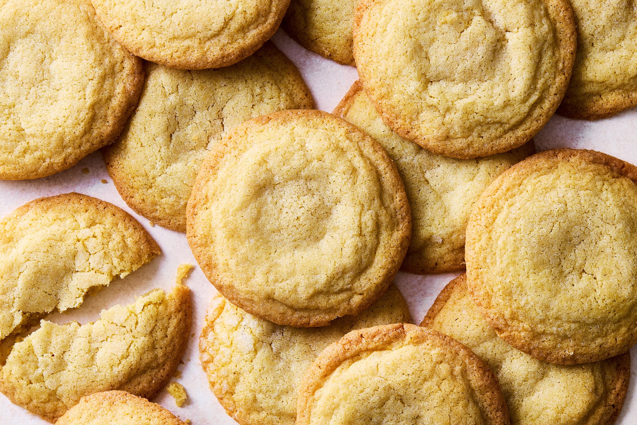 A close-up shot of a pile of golden-brown sugar cookies, with one cookie broken in half.