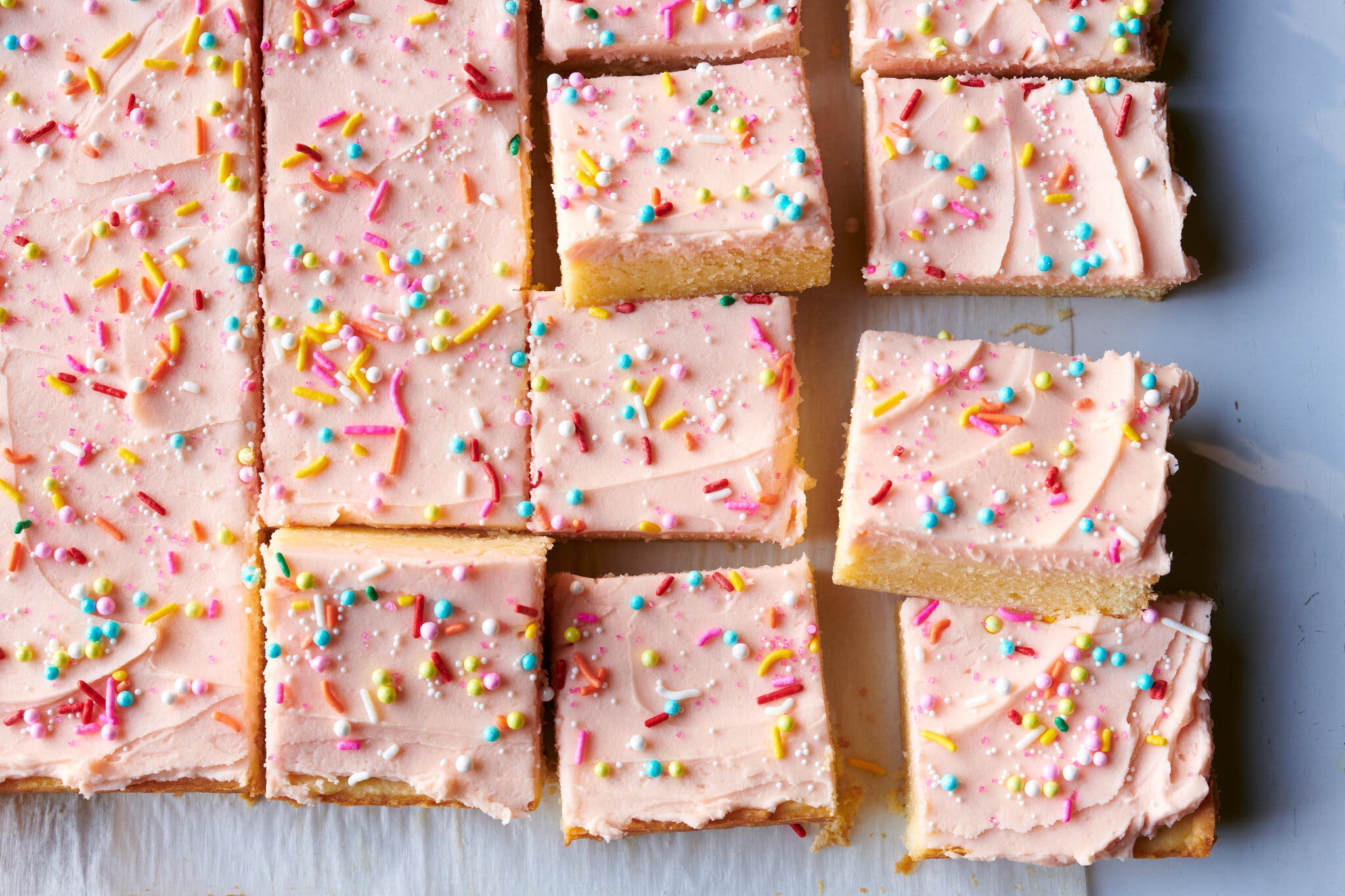 Pink frosted sugar cookie bars with colorful sprinkles, arranged on a surface.