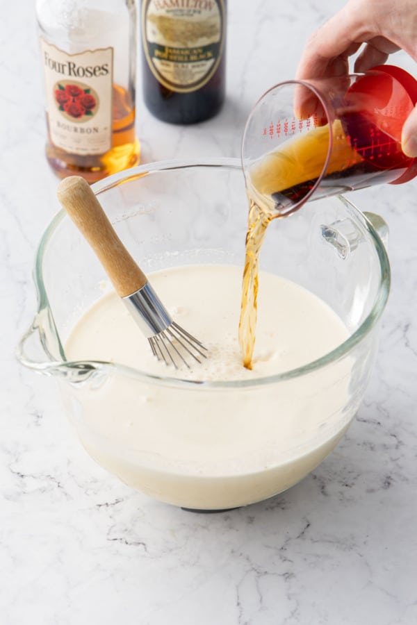 Whisking in the alcohol to the homemade eggnog in a mixing bowl.