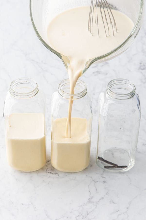 Pouring homemade eggnog into glass milk bottles with a piece of vanilla bean in each bottle.
