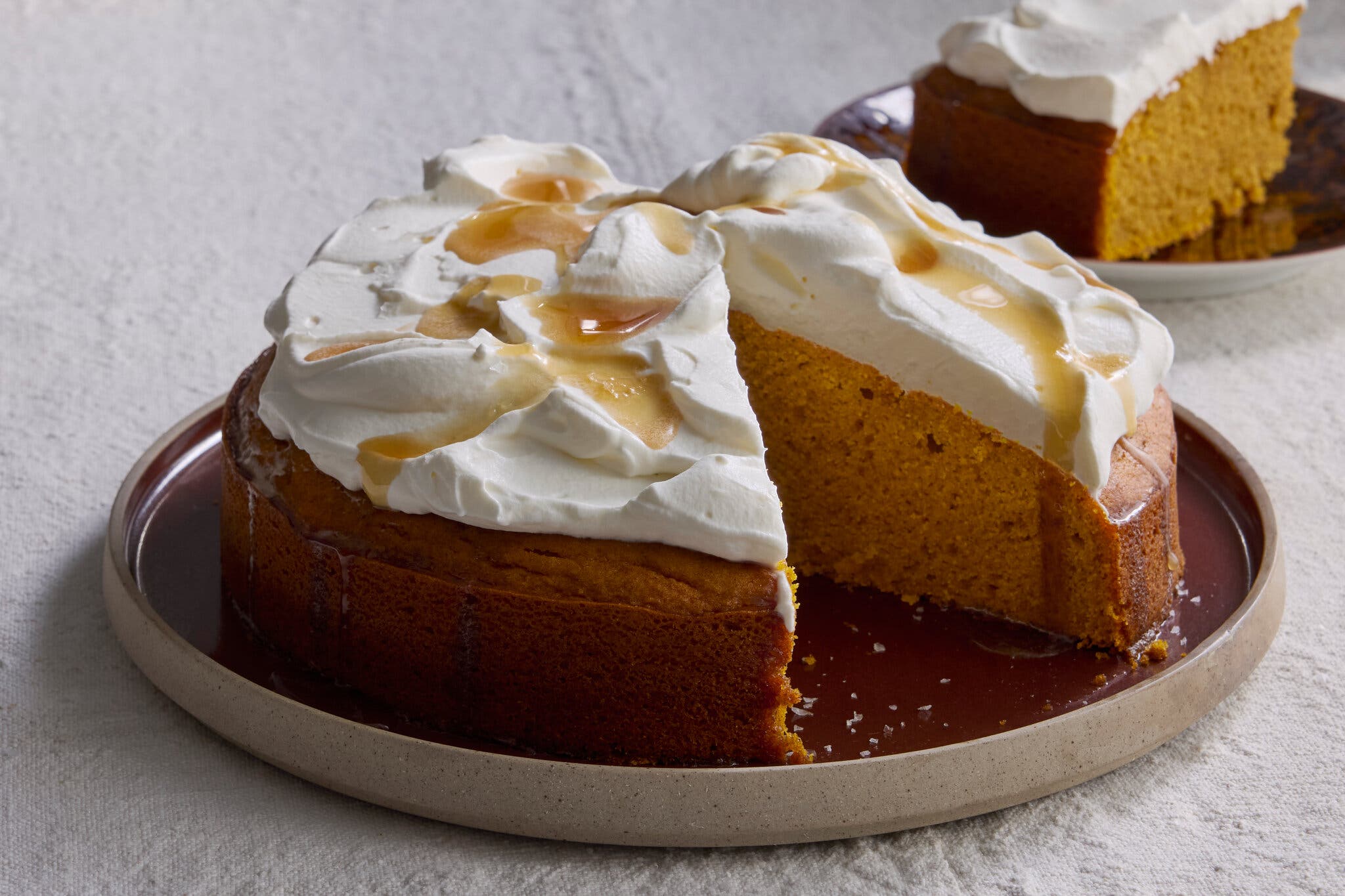 A slice has been removed from a pumpkin cake topped with whipped cream and a drizzle of sauce.