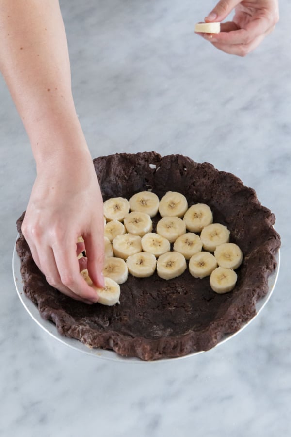 Arranging sliced bananas in the bottom of a chocolate pie crust.